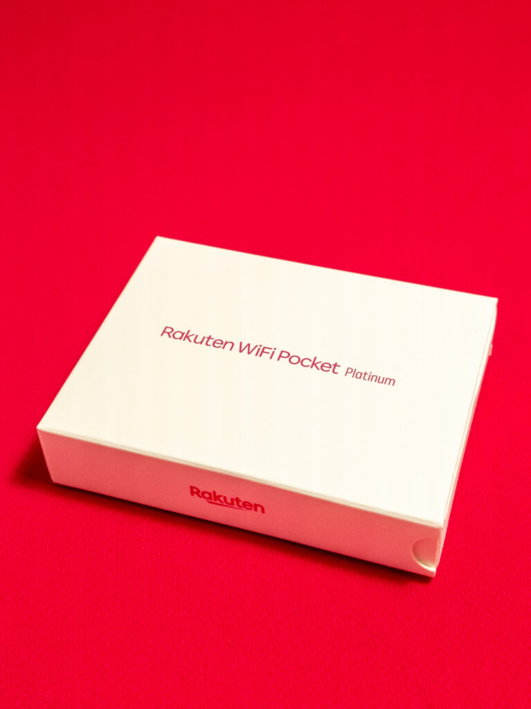 Rakuten WiFi Pocket Platinumのパッケージ画像。白い箱に製品名と楽天ロゴが印刷されており、赤い背景の上に置かれているシンプルで洗練されたデザインのパッケージ。