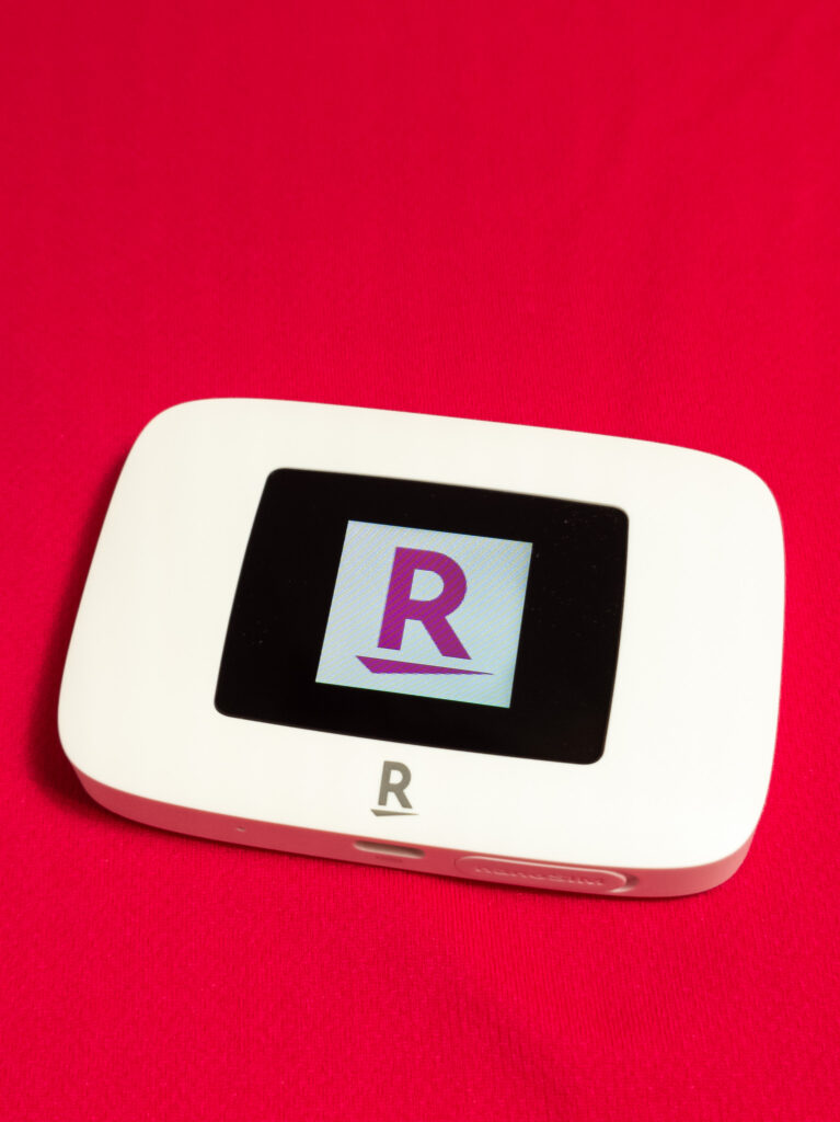 Rakuten WiFi Pocket Platinum本体の画像。赤い背景の上に置かれた白いポータブルWiFiデバイスで、画面に楽天ロゴが表示されている。